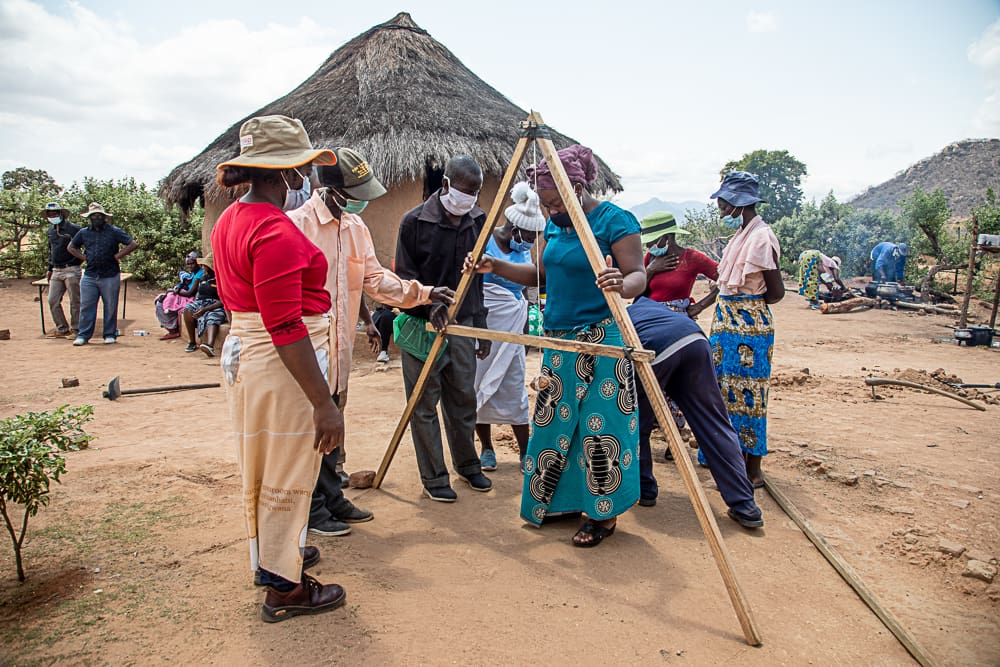 OCTOBER 07, 2021: POLITE MASARA, Disaster Risk Reduction Officer, uses a homemade A-frame to map out the flow of water at Cephas and Winnet’s homestead as BARBRA SIBANDA, Zaka District Supervisor, and community members look on. © Charmaine Chitate/ CARE